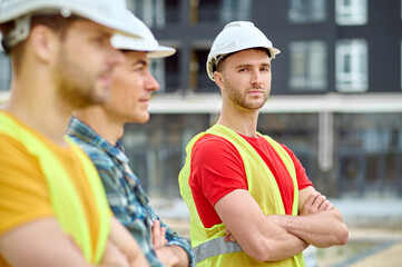 Serious builder in a safety vest accompanied by his colleagues