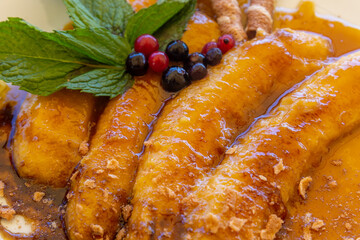 Closeup shot of fried bananas with caramel sauce decorated with berries and mint