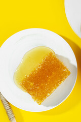 Creative layout made of Honeycombs and fresh sweet sticky honey puddle on white plate on bright yellow background. Healthy Food concept.