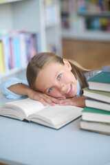 Joyous pretty schoolgirl lying on a library book