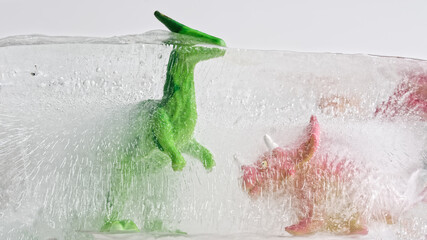 Toy dinosaurs frozen into the ice block. Educational teaching concept of ice age, extinction of dinosaurs due to climate change
