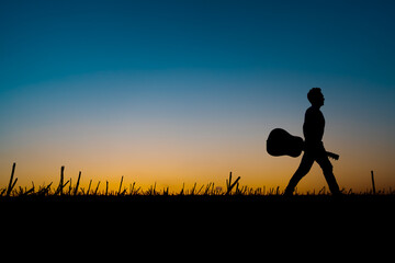 Silhouette of a musician holding a guitar and walking along the horizon at sunset