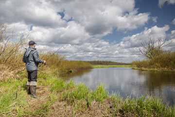 Fisherman throws spinning rod on the river bank.