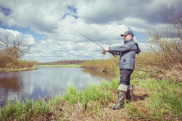 Fisherman in a jacket throws a spinning rod.