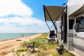 Panoramic view of many surf board kite riders on sand beach watersport spot on bright sunny day against rv camper van vehicle at sea ocean coast at surfing camp. Fun adventure travel sport acitivity - obrazy, fototapety, plakaty