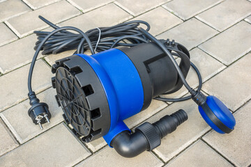 Submersible electric pump with a blue plastic housing on a stone floor - obrazy, fototapety, plakaty