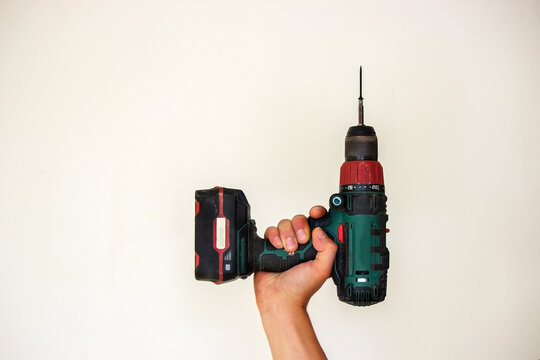 Hand with cordless screwdriver and drill isolated on white background. Twists screws into the board.