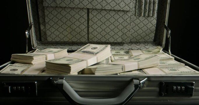 Packs of cash falling into a metal case filled with money. 100 dollar bills in a briefcase. Finance, investing, business concept close up 4k footage