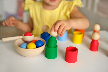 Fototapeta na wymiar A sorter toy. Children's educational games.The child learns colors by playing with toy multi-colored wooden cylinders in the shape of a man and inserting them into cups of the appropriate color.