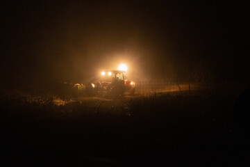 Street lamp and a tractor in a field during nighttime