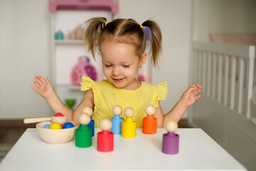 The girl learns colors by playing with wooden cylindrical toy colored human figures and placing...