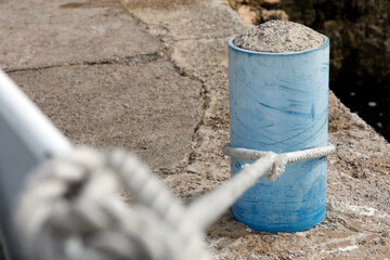 Bollard with rope and knot on the harbor quay, close up.