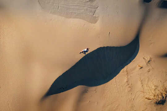 Woman lie on wavy sand dunes in desert landscape at golden sunset light and wind.