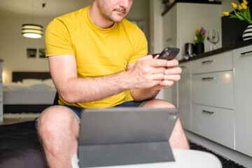 Naklejka na ściany i meble Man chatting with friends within smartphone and tablet sitting in the kitchen 