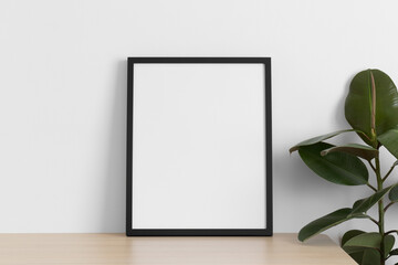 Black frame mockup on the wooden table with a ficus plant.