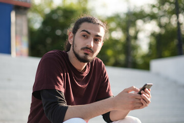 Fototapeta premium Close up portrait of handsome Arab man walking in the park and using smartphone