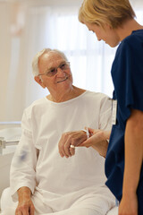 Nurse reading older patient's medical bracelet in hospital