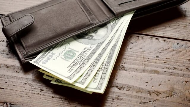 Hand counting money in leather wallet on wooden table in 4K VIDEO. One hundred US banknotes. Cash of hundred dollar bills, paper money currency.