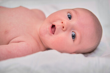 Portrait of a smiling infant baby lying on the bed, close-up. Happy baby boy, face closeup