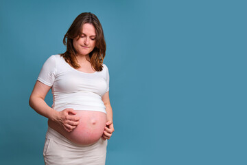 Portrait of a pregnant woman scratching her stomach, blue background