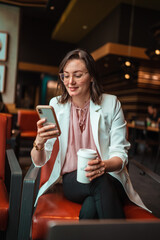 woman using her phone and holding her coffee in a coffee shop