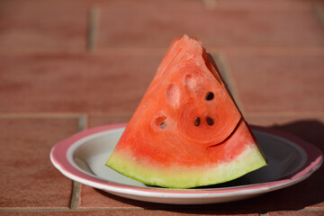 A piece of fresh red watermelon, with a green skin, arranged on a plate for eating