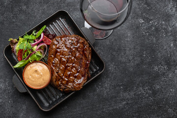 Grilled pork steak with sauce, glass of wine and vegetables in a frying pan with place for text