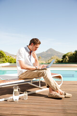 Man using laptop on lounge chair at poolside