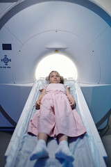 Little girl lying on long medical table and moving into mri scan machine in modern clinics