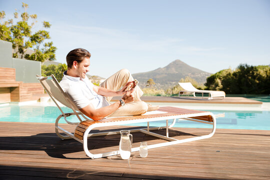 Man using digital tablet on lounge chair at poolside