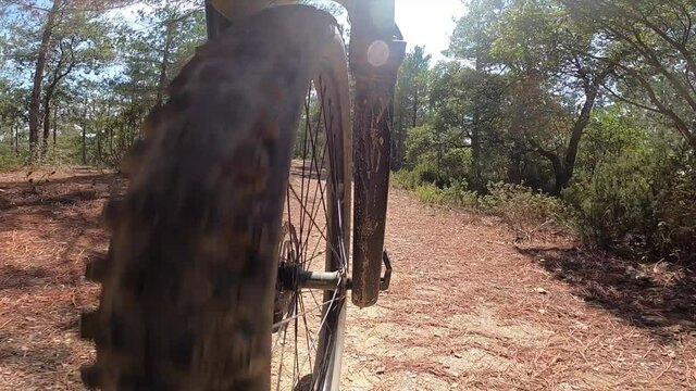 Riding an off road mountain bike front wheel point of view on a gravel path in a forest