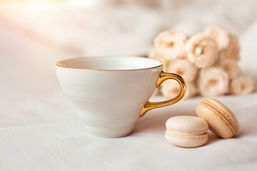 Sweet dessert, vanilla macaroons, mug and white roses on bed background. Romantic morning breakfast at bed.