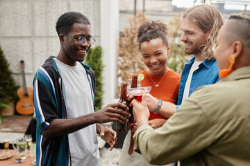Waist up shot of carefree young people clinking drinks while enjoying outdoor party with friends