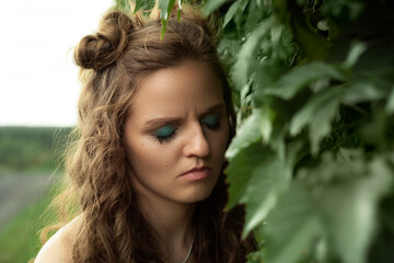 Naklejka premium Portrait of a beautiful curly girl with closed eyes in green foliage