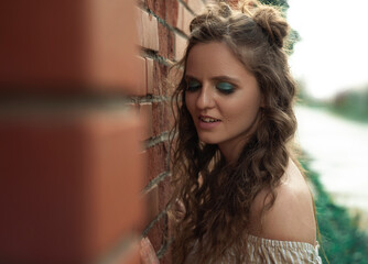 Young beautiful curly girl stands next to a brick wall