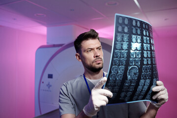 Contemporary radiologist in gloved and uniform looking at x-ray image of mri scan examination of...