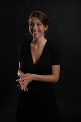 A young beautiful woman happy and smiling in a studio shot in black dress and background looking at the camera