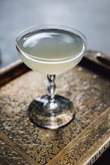 white cloudy cocktail in vintage etched coupe glass stemware on gold brass Indian tray 