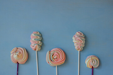 meringue on a stick. meringue of pastel colors. do-it-yourself tender dessert. puffs on a blue background. top view, flat lay