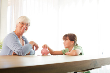 Older woman and granddaughter filling piggy bank