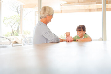 Obraz premium Older woman and granddaughter filling piggy bank