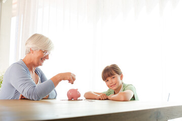 Older woman and granddaughter filling piggy bank
