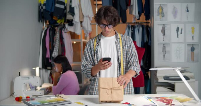 Fashion designer pack new clothes in box before delivering in workshop and take photo on cellphone