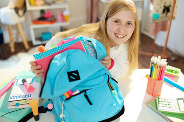 happy school girl packing for school at home in sunny day