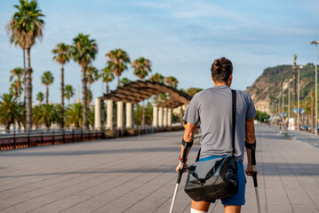 Unrecognizable young man with crutches walking in the city