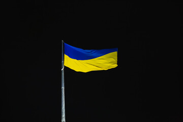 Ukraine flag fluttering in the wind against black night sky. National Ukrainian symbol - yellow and blue colors.