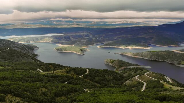 Wide view of water reservoir and its surroundings under the shadows of thick clouds.