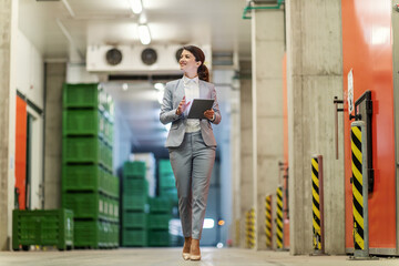 Owner visiting the warehouse, business control. A woman looks good in an elegant suit walking through the hallways while checking the state of business on a tablet she is holding in her hand. CEO