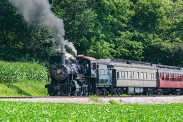 Fototapeta na wymiar View of an Antique Restored Steam Passenger Train Blowing Smoke and Steam on a Sunny Summer Day