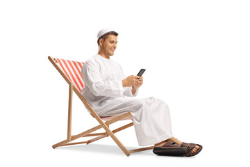 Young man in ethnic clothes sitting in a beach chair with a mobile phone